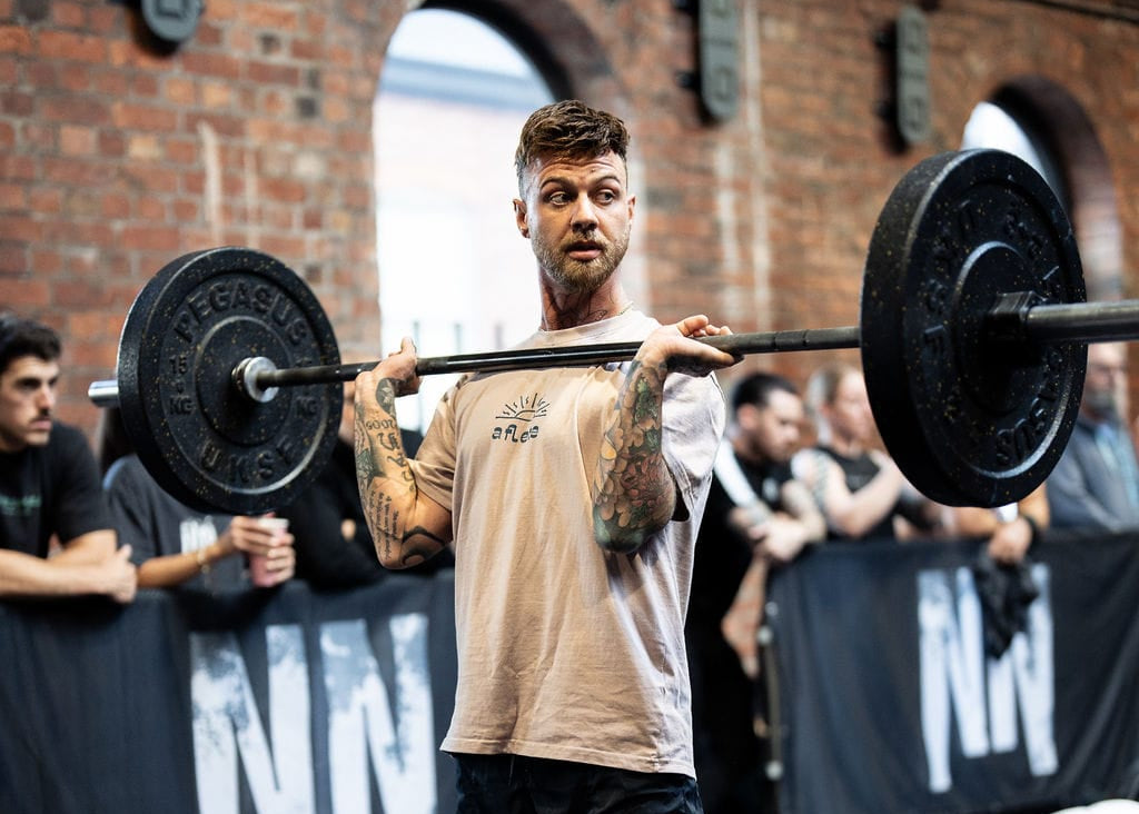 Man lifting a barbell in a gym setting with spectators in the background